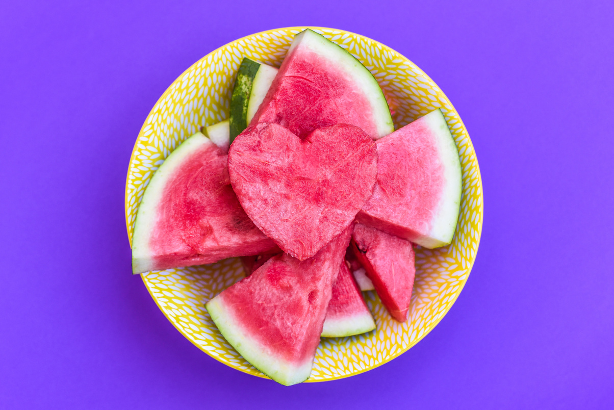 Tasty sliced watermelon in yellow bowl with purple background and with heart-shaped slice on top
